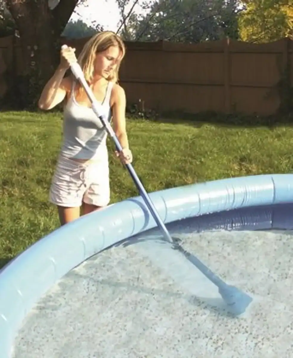 Child using a pool vacuum cleaner to clean the pool.