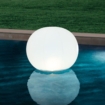 Floating lamp in the shape of a large white ball floats on the pool water.