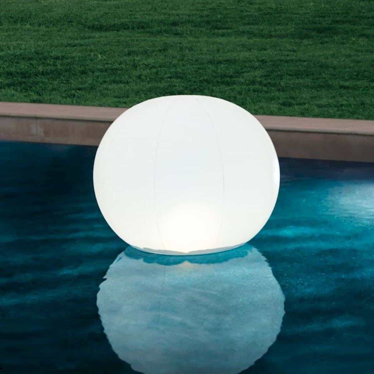 Floating lamp in the shape of a large white ball floats on the pool water.